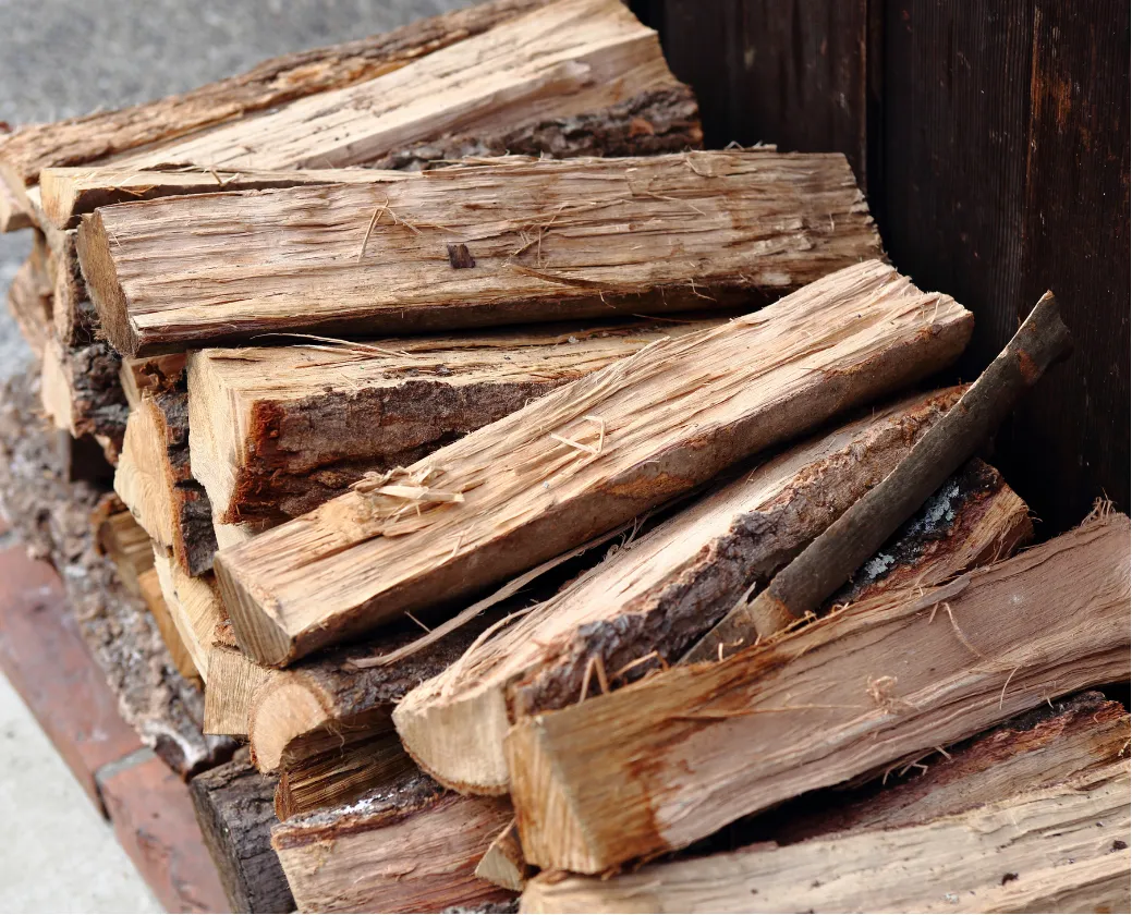 A stack of chopped firewood logs neatly piled next to a wooden wall outdoors.