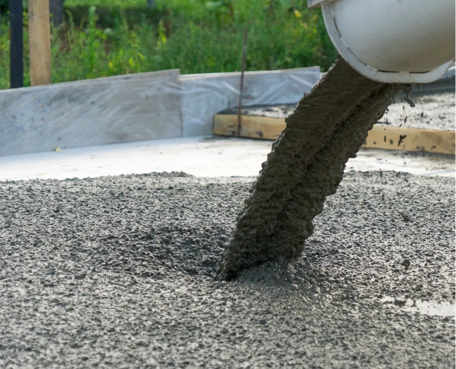 Wet concrete pouring from a chute onto a construction site foundation with wooden forms in the background.